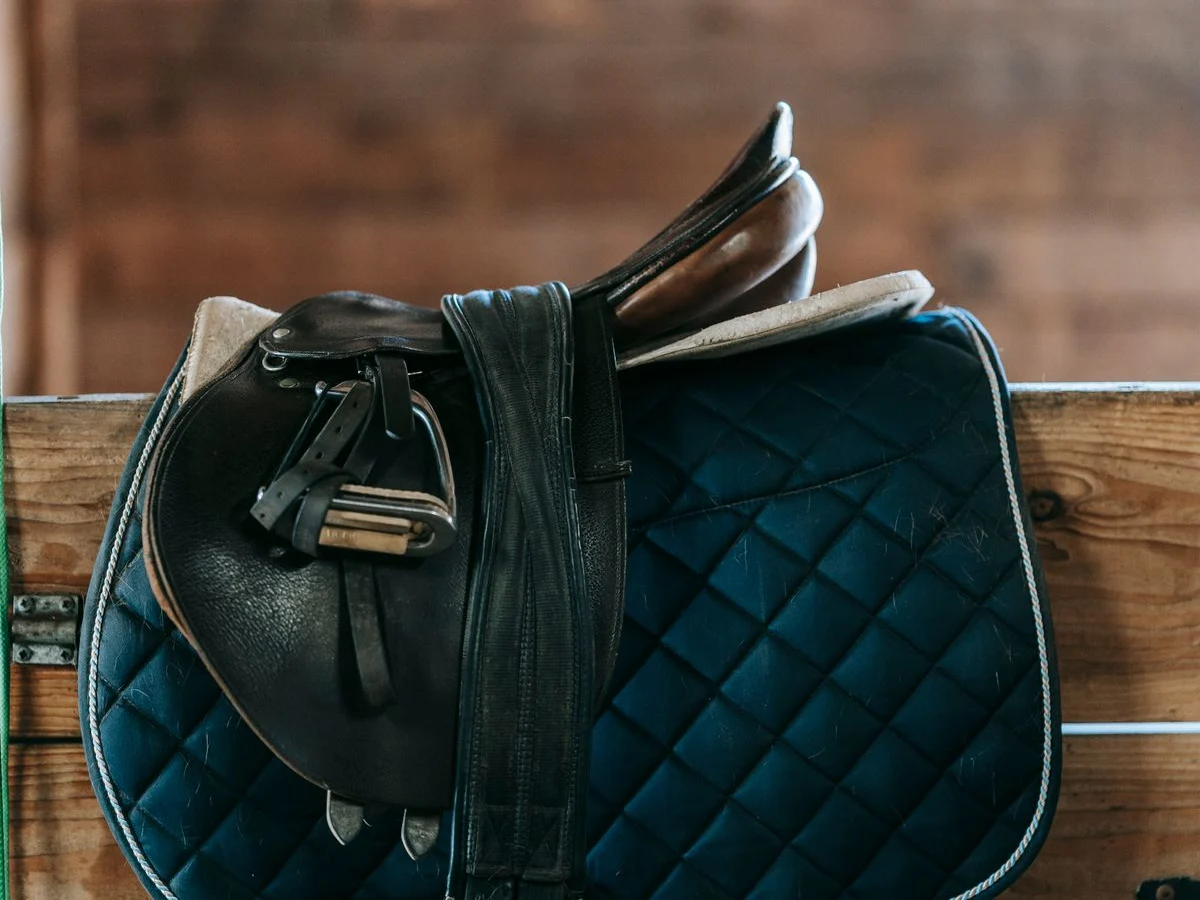 An English saddle with its seat, flap, stirrup leather and iron visible above a blue saddle pad.
