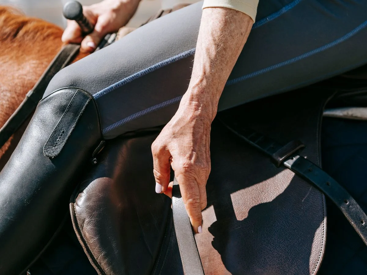 A rider handles a stirrup leather beside the saddle.