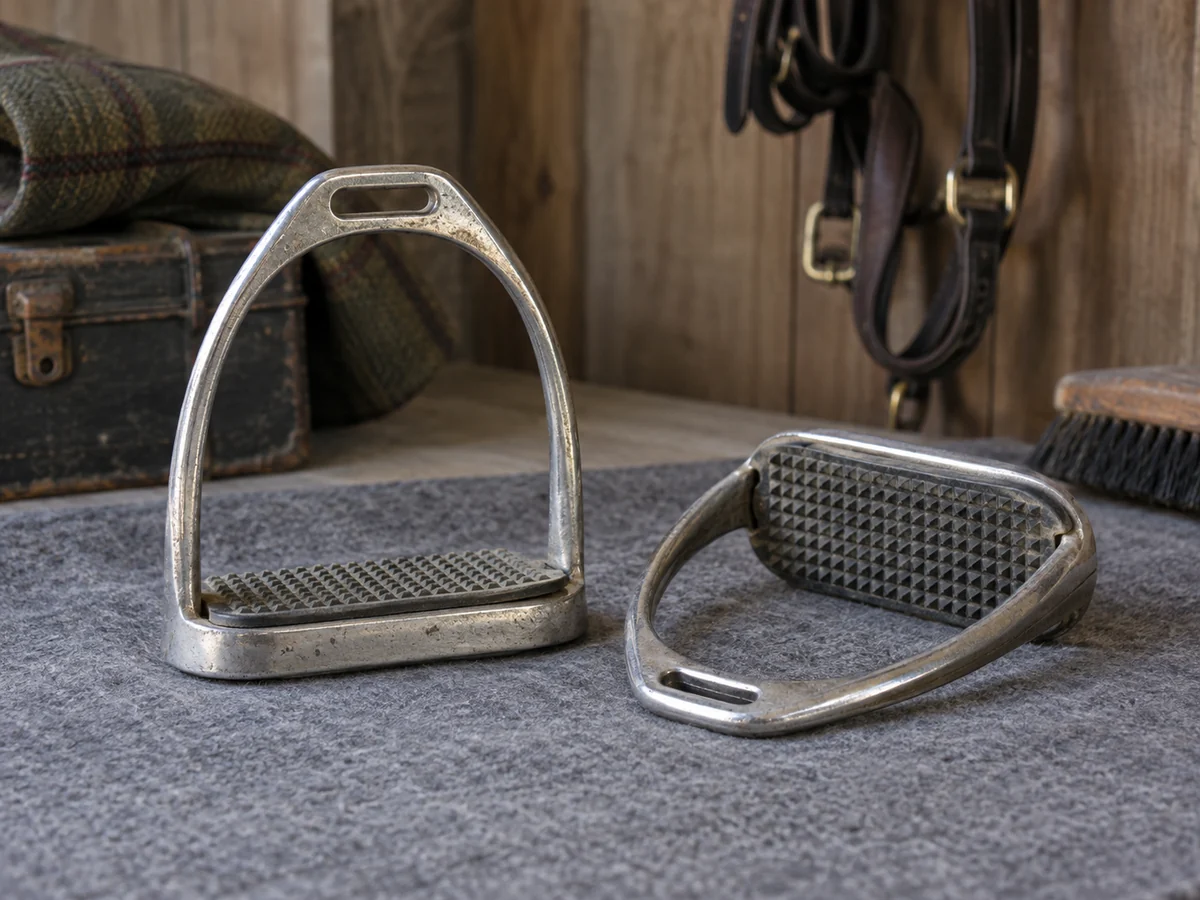 A pair of used metal English stirrups on a grey mat.