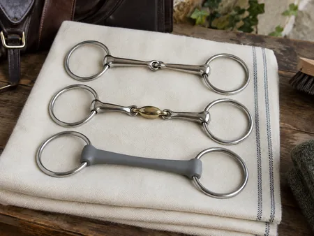 Three clean equestrian snaffle bits neatly separated on folded ivory cloth: single joint.