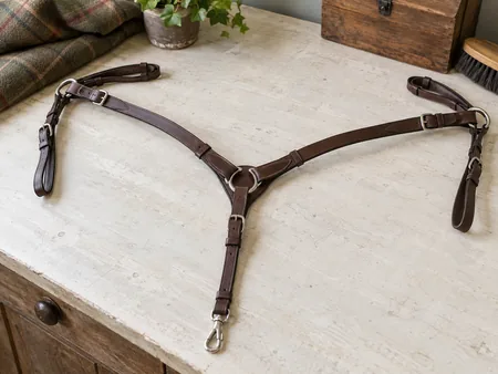 A complete plain brown leather three-point horse breastplate neatly arranged on an off-white work surface.