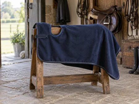 A neatly spread navy fleece quarter sheet with a saddle cut-out on a wooden saddle stand.