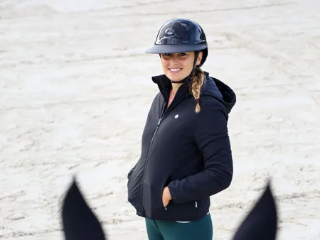 A rider wears a fitted jacket, riding trousers and helmet at an outdoor arena.