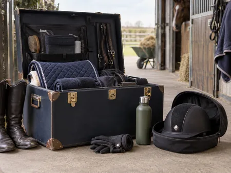 An open equestrian kit trunk beside a separately protected riding helmet.