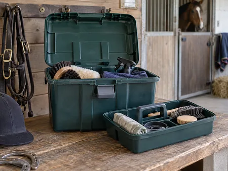 A sturdy open plastic tack box with removable tray and carry handle on a clean stable bench.