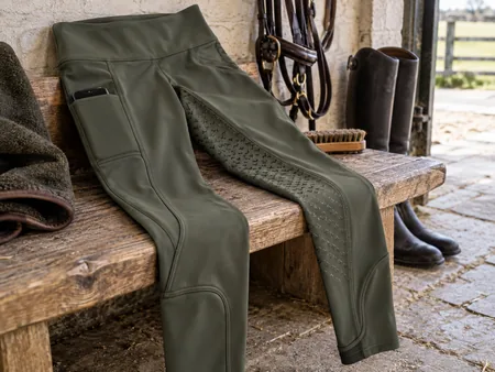 A pair of dark olive equestrian riding tights neatly laid on a bench.