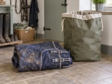 A muddy navy horse rug folded beside a large laundry sack in a practical utility room.