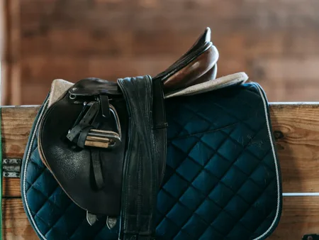 An English saddle with its seat, flap, stirrup leather and iron visible above a blue saddle pad.