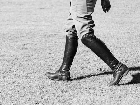 Tall black riding boots and breeches photographed on grass.