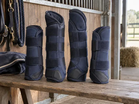 A complete set of four navy horse travel boots standing loosely on a stable bench.