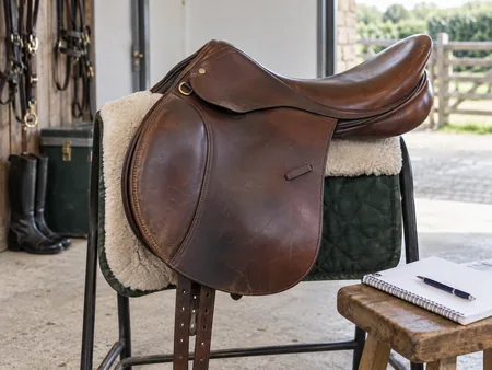 A gently used brown English saddle on a padded stand beside a small notebook.