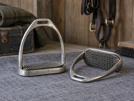 A pair of used metal English stirrups on a grey mat.